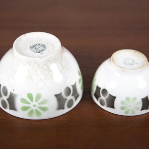 May include: Two white ceramic bowls with black and green geometric designs. The larger bowl has a worn, distressed look. Both bowls have a circular mark on the bottom.
