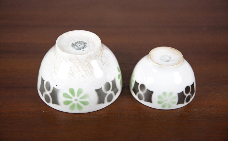May include: Two white ceramic bowls with black and green geometric designs. The larger bowl has a worn, distressed look. Both bowls have a circular mark on the bottom.
