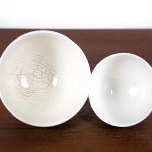 May include: Two white ceramic bowls, one larger than the other, with a crackled glaze. The larger bowl has a more pronounced crackle pattern.