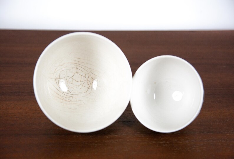 May include: Two white ceramic bowls, one larger than the other, with a crackled glaze. The larger bowl has a more pronounced crackle pattern.