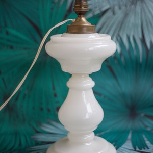 May include: A white ceramic table lamp with a brass base and a white cord. The lamp is sitting on a green and white patterned surface.