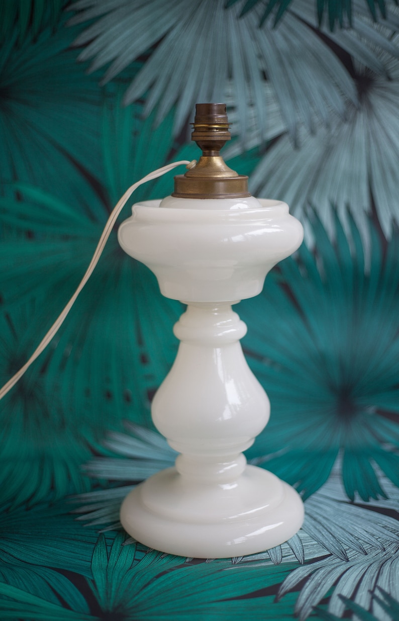 May include: A white ceramic table lamp with a brass base and a white cord. The lamp is sitting on a green and white patterned surface.