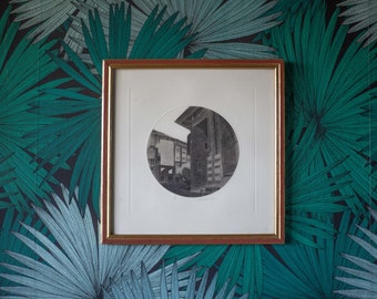 May include: A framed black and white photograph of a building with a circular window. The frame is gold with a red mat. The photograph is set against a green and blue palm leaf patterned background.