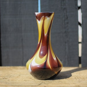 Könnte beinhalten: Eine braune und gelbe Glasvase mit einem Wirbelmuster. Die Vase hat einen schmalen Hals und einen breiten Boden.