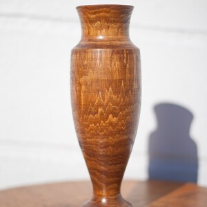 Peut inclure: Un vase en bois avec une finition en bois naturel brun. Le vase a une base large et un col &eacute;troit.