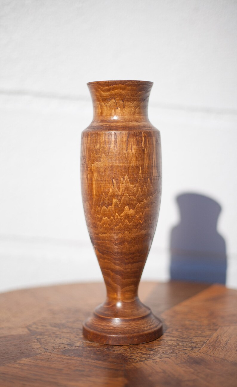 Peut inclure: Un vase en bois avec une finition en bois naturel brun. Le vase a une base large et un col &eacute;troit.