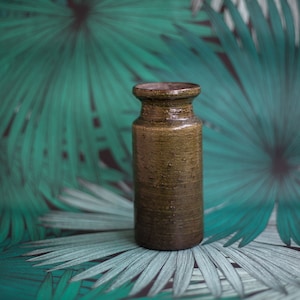 May include: A brown ceramic vase with a textured surface sits on a green and white patterned background.