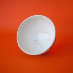 May include: A white ceramic bowl with a crackled glaze. The bowl is empty and sitting on a bright orange surface.