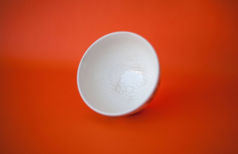 May include: A white ceramic bowl with a crackled glaze. The bowl is empty and sitting on a bright orange surface.