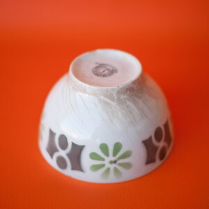 May include: White ceramic bowl with a brown, green, and white geometric design. The bowl has a slightly textured surface and a small brown stamp on the bottom.