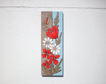Könnte beinhalten: Eine Keramikfliese mit einem Blumendesign. Die Fliese zeigt rote und weiße Blumen mit grünen Blättern auf einem braunen und blauen Hintergrund.