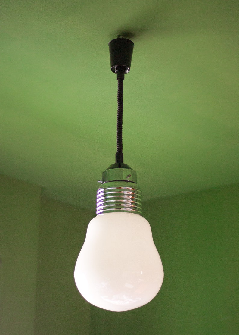 May include: A white light bulb hangs from a black cord and a silver ceiling fixture against a green wall.