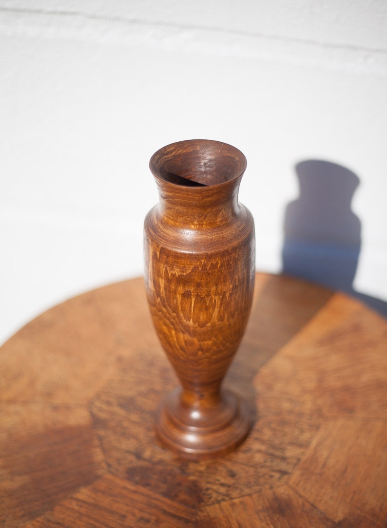 Peut inclure: Un vase en bois avec une finition teint&eacute;e brune. Le vase a une base arrondie et un col &eacute;troit.