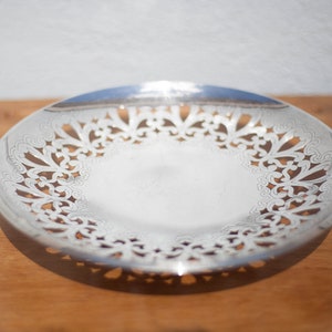 May include: A silver serving dish with a decorative, openwork design around the edge. The dish is on a wooden surface.