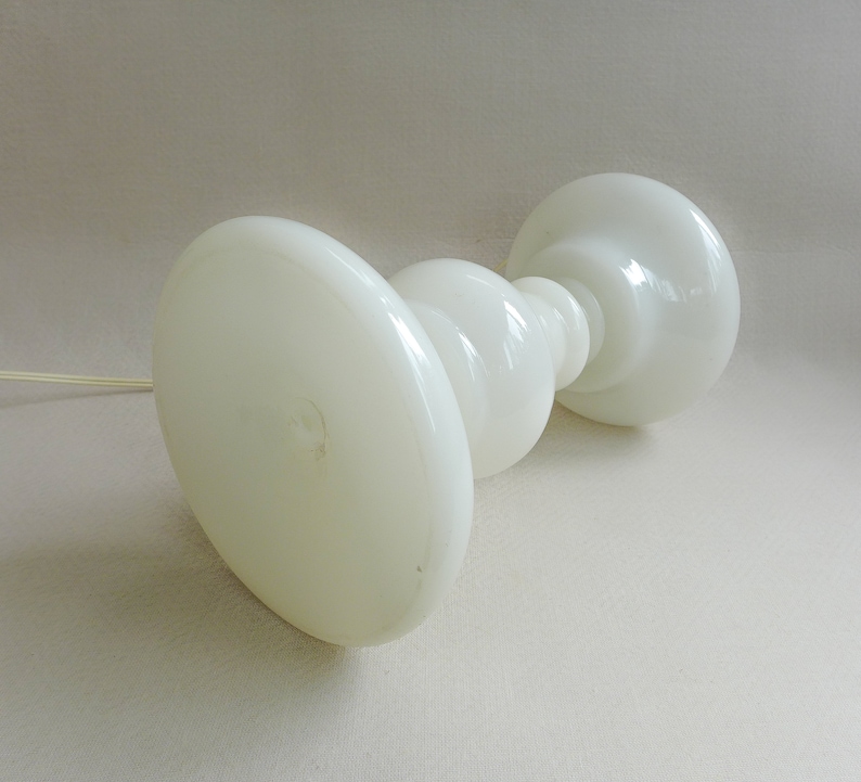 May include: White glass table lamp with a rounded base and a wide, flat top. The lamp has a simple, modern design.