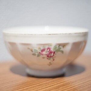 K&ouml;nnte beinhalten: Eine wei&szlig;e Keramiksch&uuml;ssel mit einem Blumendesign mit rosa und roten Blumen. Die Sch&uuml;ssel hat einen geriffelten Rand und steht auf einer Holzoberfl&auml;che.