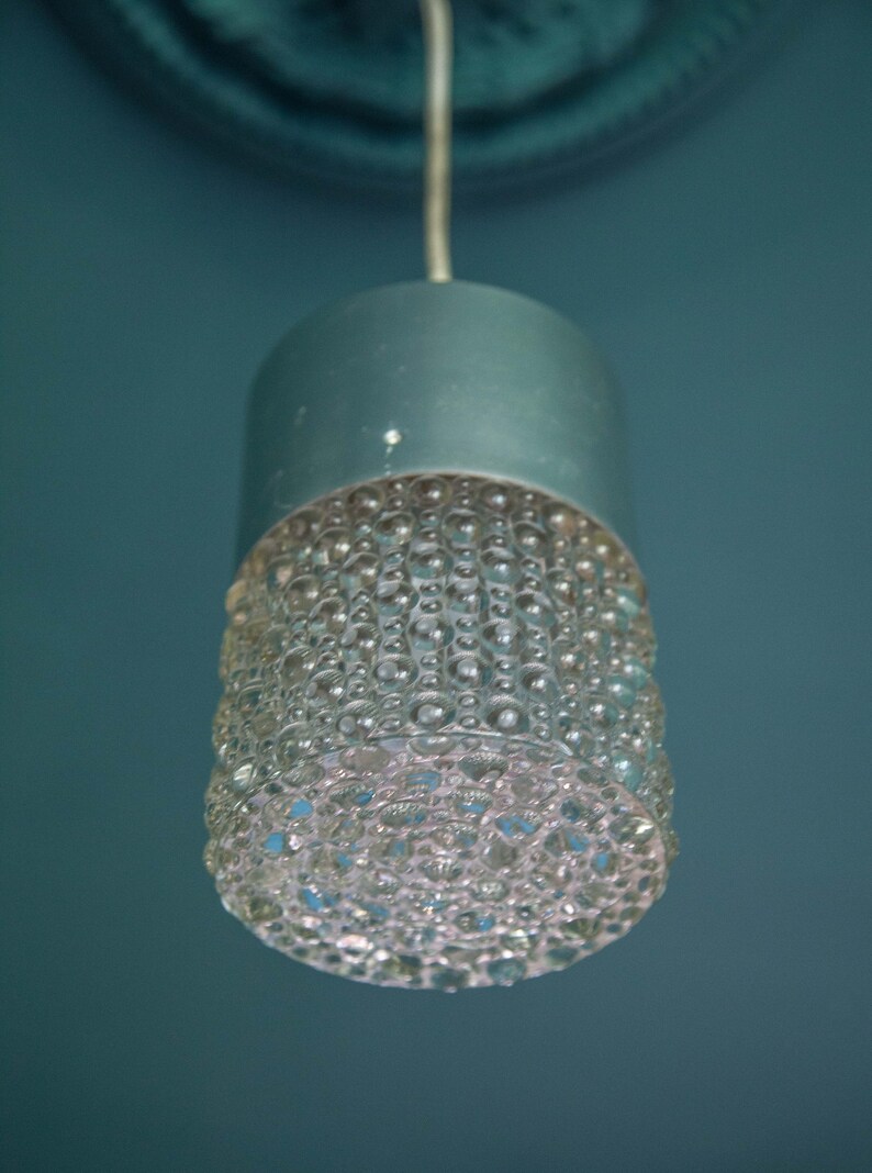K&ouml;nnte beinhalten: Eine silberne Pendelleuchte mit einem klaren Glasschirm, der ein strukturiertes Muster aus kleinen Blasen aufweist.