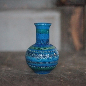 Peut inclure: Petit vase en céramique bleu, corps arrondi et col étroit. La surface texturée présente des motifs horizontaux et pointillés dans des tons de bleu et de vert. Le vase mesure environ 15 cm de haut.