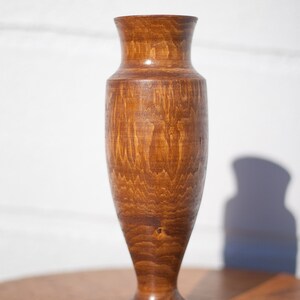 Peut inclure: Un vase en bois avec une finition teint&eacute;e brune. Le vase a un corps arrondi et une base &eacute;vas&eacute;e.
