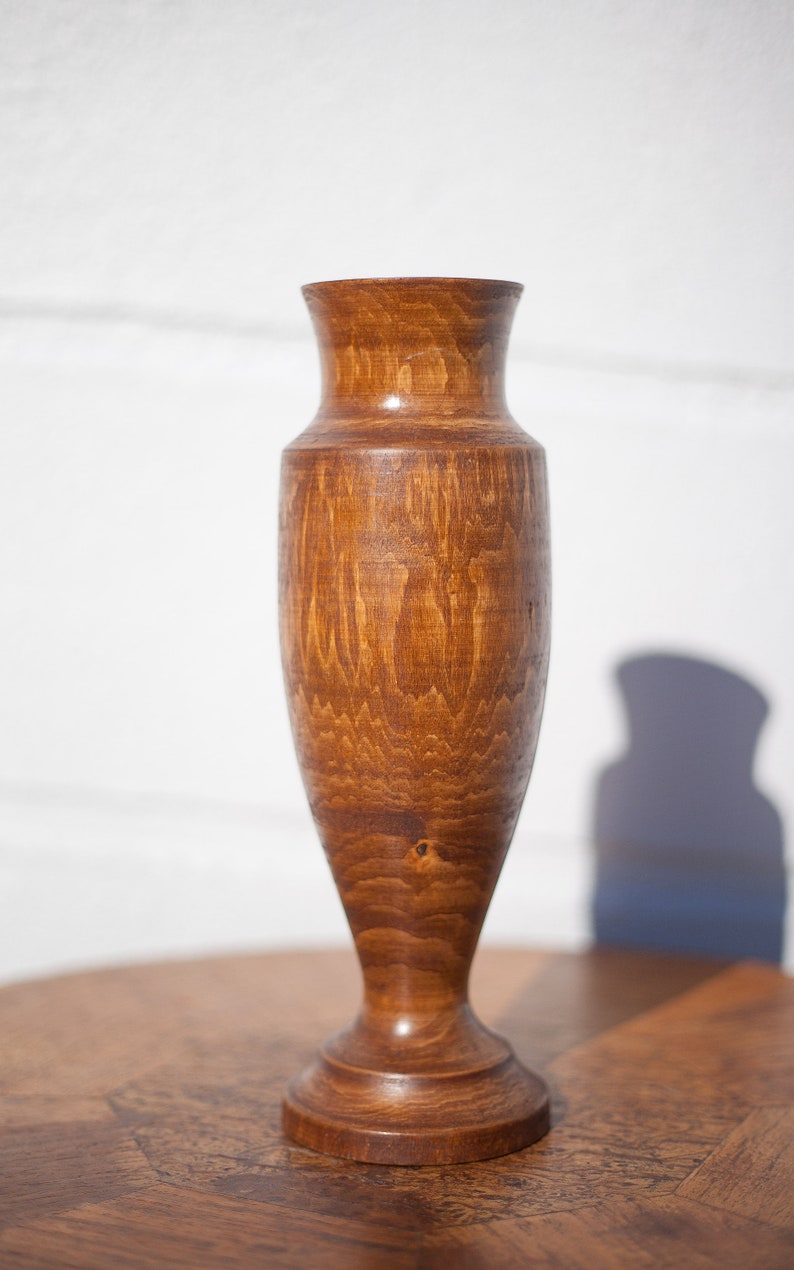 Peut inclure: Un vase en bois avec une finition teint&eacute;e brune. Le vase a un corps arrondi et une base &eacute;vas&eacute;e.