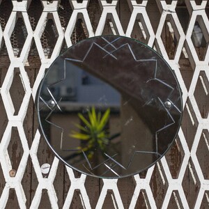 May include: A round, black mirror with a starburst design is mounted on a white, diamond-shaped lattice wall.