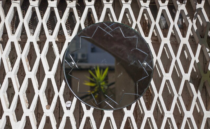 May include: A round, black mirror with a starburst design is mounted on a white, diamond-shaped lattice wall.