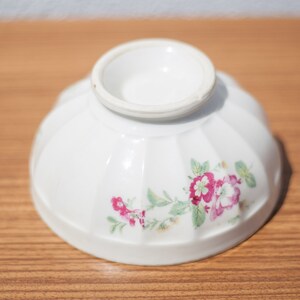 K&ouml;nnte beinhalten: Eine wei&szlig;e Keramiksch&uuml;ssel mit Blumenmuster. Die Sch&uuml;ssel hat einen geriffelten Rand und ein wei&szlig;es Innere. Das Blumenmuster zeigt rosa und gr&uuml;ne Blumen.