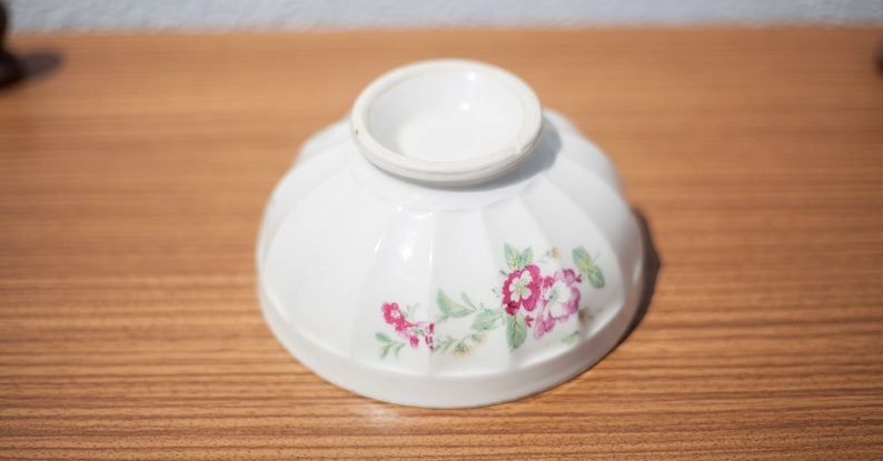 K&ouml;nnte beinhalten: Eine wei&szlig;e Keramiksch&uuml;ssel mit Blumenmuster. Die Sch&uuml;ssel hat einen geriffelten Rand und ein wei&szlig;es Innere. Das Blumenmuster zeigt rosa und gr&uuml;ne Blumen.