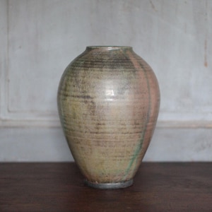 Peut inclure: Un vase en céramique artisanal, avec un corps arrondi et un col étroit. Le vase présente un mélange de tons terreux, notamment beige, marron et des touches de rose et de vert. Le vase mesure environ 25 cm de haut et a une esthétique rustique et artisanale.