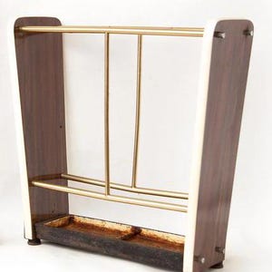 May include: Vintage umbrella stand with a dark wood finish and brass accents. The stand has a rectangular base with a built-in tray and a series of brass bars for holding umbrellas. The sides are a dark wood with cream-colored trim.