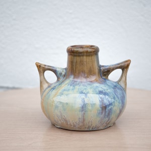 May include: A small, ceramic vase with two handles. The vase is decorated with a blue, green, and brown glaze.
