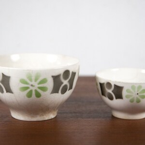 May include: Two white ceramic bowls with a black and green geometric pattern. The larger bowl is slightly wider and taller than the smaller bowl.