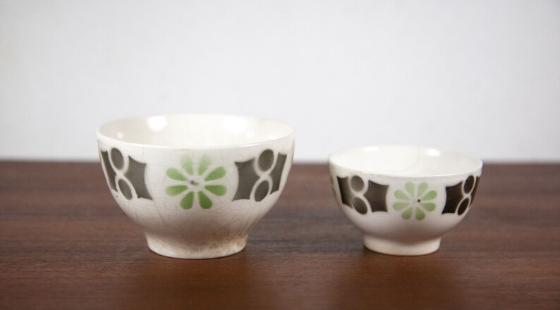 May include: Two white ceramic bowls with a black and green geometric pattern. The larger bowl is slightly wider and taller than the smaller bowl.