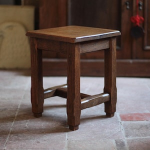 Pode incluir: Um pequeno banco quadrado de madeira com acabamento castanho escuro. O banco tem quatro pernas conectadas por um suporte inferior e um tampo plano. O design é simples e clássico, adequado para vários estilos de interiores. Dimensões: aprox. 30 cm x 30 cm.