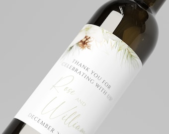 May include: A dark glass wine bottle with a white label featuring a pine cone and greenery illustration. The text reads: THANK YOU FOR CELEBRATING WITH US! Rose AND William DECEMBER 23, 2023. The label has a clean, white background.
