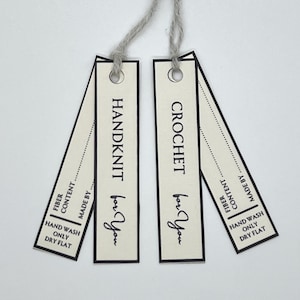 Op de afbeelding: Twee crèmekleurige rechthoekige labels met grijs touw, met de tekst "HANDKNIT for You" en "CROCHET for You" in een handschriftachtig lettertype. Elk label bevat "FIBER CONTENT", "MADE BY" en verzorgingsinstructies: "HAND WASH ONLY DRY FLAT".