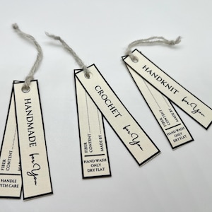 Op de afbeelding: Drie off-white rechthoekige labels met zwarte randen en grijs touw. De labels lezen "HANDMADE for You", "CROCHET for You" en "HANDKNIT for You" in zwarte tekst. Elk label bevat onderhoudsinstructies en informatie over de vezelinhoud.