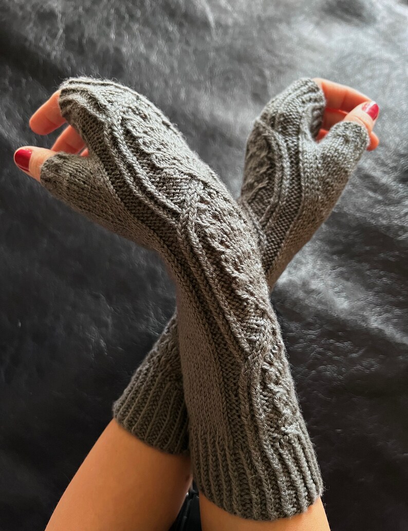 May include: A pair of gray fingerless gloves with a cable knit pattern.