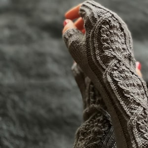 May include: A pair of gray fingerless gloves with a detailed knit pattern. The gloves are made with a soft yarn and have a comfortable fit.