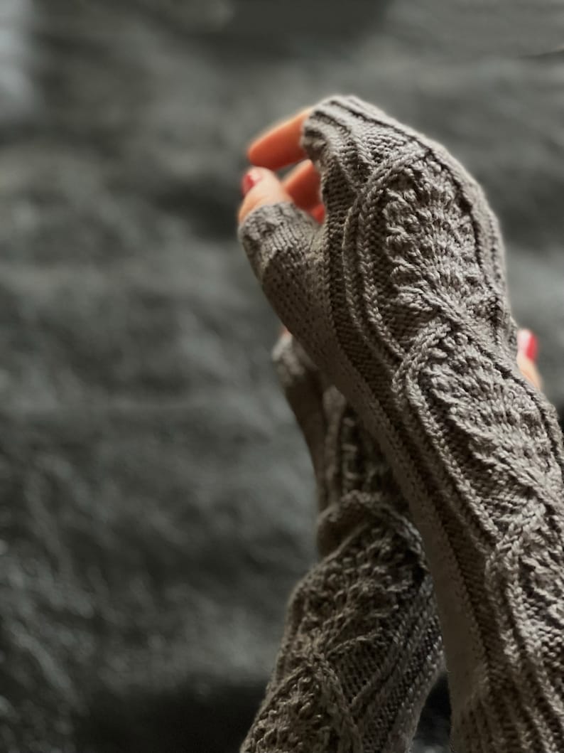 May include: A pair of gray fingerless gloves with a detailed knit pattern. The gloves are made with a soft yarn and have a comfortable fit.