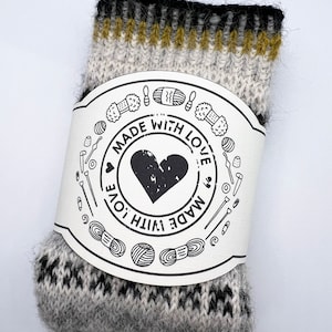 May include: A pair of gray and black knit socks with a yellow stripe at the top. The socks are packaged with a white label that says "Made with Love" in a circle with a heart in the center.