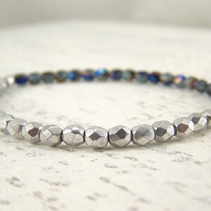 May include: A silver and blue beaded bracelet with faceted beads. The bracelet is made with small, round beads that are arranged in a graduated pattern.