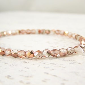 May include: A delicate bracelet made with rose gold and clear glass beads. The bracelet has a simple design and features small silver charms.