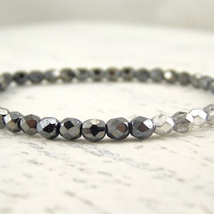 May include: A bracelet made of small, faceted, grey hematite beads. The beads have a metallic sheen and are strung together. The bracelet is designed to be worn around the wrist. The beads are approximately 0.3 cm in diameter.