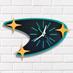 May include: A teal and black mid-century modern clock with gold star accents. The clock is shaped like a boomerang and has a white face with black hour and minute hands.