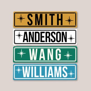 May include: Four rectangular metal signs with rounded corners and small holes at each end. The signs feature the names SMITH in black on gold, ANDERSON in black on white, WANG in white on green, and WILLIAMS in white on blue, each with star icons.