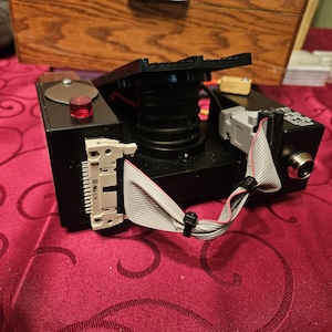 May include: A black and gray camera with a red button and a black cable. The camera has a black bellows and a white connector with the text "6-Pin 2.54".