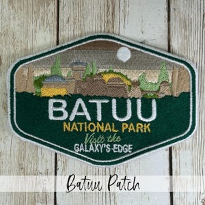 May include: Embroidered patch with a green and brown design. The patch features the text "BATUU NATIONAL PARK" and "Visit the GALAXY'S EDGE". The patch has a white border and depicts a landscape with buildings and spires.