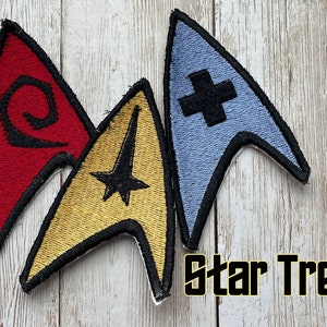 May include: Three embroidered Star Trek patches in red, gold, and blue. The red patch has a black swirl design, the gold patch has a black star, and the blue patch has a black cross. The words "Star Trek" are in a yellow font.