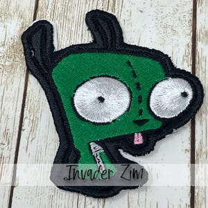 May include: Embroidered patch featuring a green alien character with large white eyes, black antennae, and a pink tongue. The patch has the text "Invader Zim" in a stylized font.
